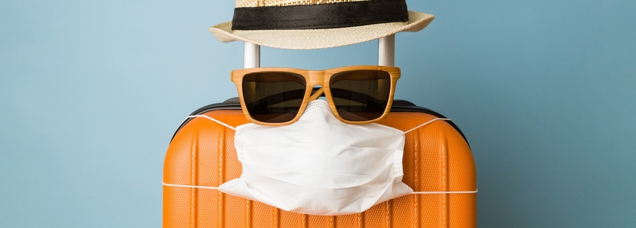 Koffer met hoed, zonnebril en beschermend medisch masker op blauwe achtergrond